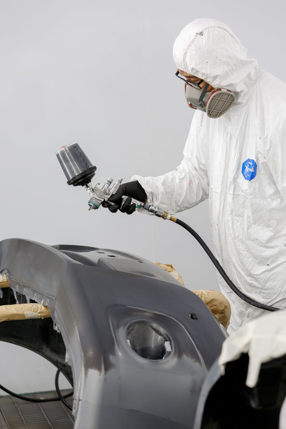 Técnico pintando una pieza de carrocería con pistola de pintura en cabina